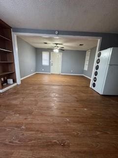 unfurnished living room featuring a textured ceiling, built in shelves, wood finished floors, a ceiling fan, and baseboards