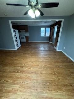 unfurnished living room with ceiling fan, baseboards, and wood finished floors