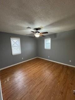 empty room featuring a textured ceiling, wood finished floors, a ceiling fan, and baseboards