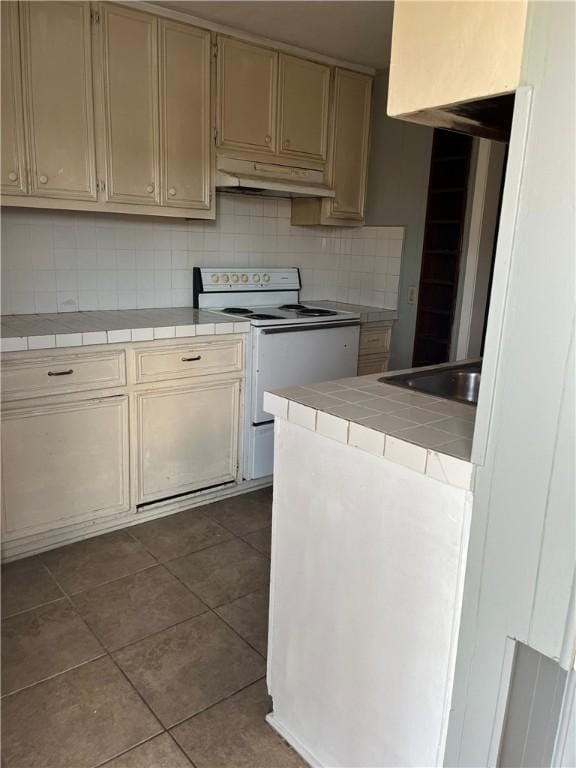 kitchen featuring electric range, tile counters, decorative backsplash, dark tile patterned flooring, and under cabinet range hood