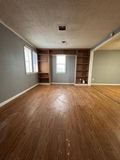 unfurnished living room featuring built in features, visible vents, baseboards, wood finished floors, and a textured ceiling