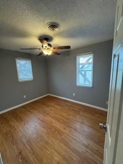 unfurnished bedroom featuring visible vents, a textured ceiling, baseboards, and wood finished floors