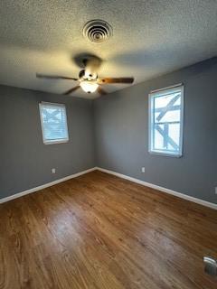 empty room with baseboards, wood finished floors, visible vents, and a healthy amount of sunlight