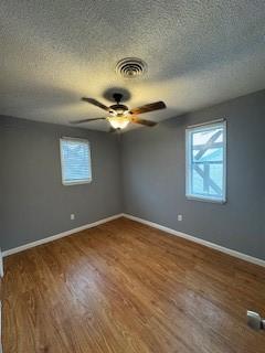 spare room featuring visible vents, ceiling fan, baseboards, and wood finished floors