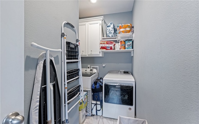 clothes washing area with cabinet space, separate washer and dryer, and a textured wall