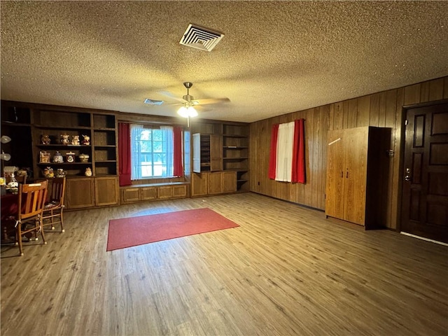 interior space with wood walls, wood finished floors, visible vents, a ceiling fan, and a textured ceiling