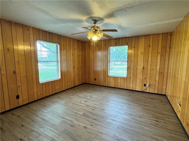 unfurnished room with a ceiling fan, wood walls, a healthy amount of sunlight, and wood finished floors