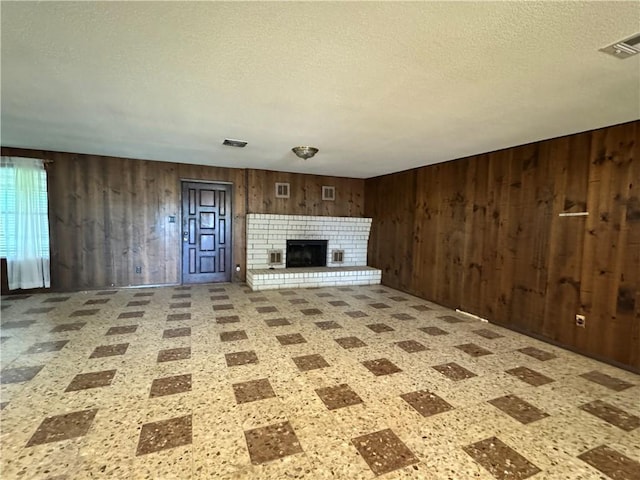 unfurnished living room with visible vents, tile patterned floors, wood walls, and a textured ceiling