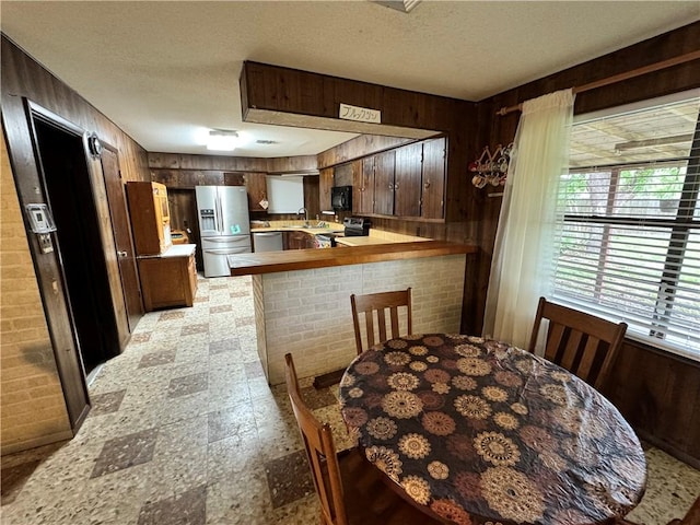 kitchen with stainless steel appliances, a peninsula, a sink, a textured ceiling, and wooden walls