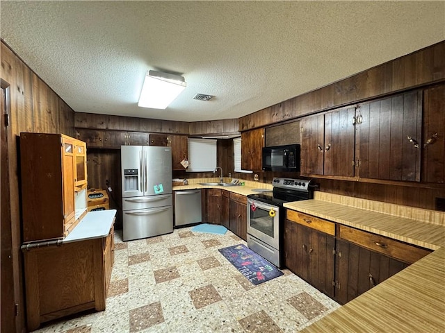 kitchen with light floors, light countertops, wooden walls, a sink, and appliances with stainless steel finishes