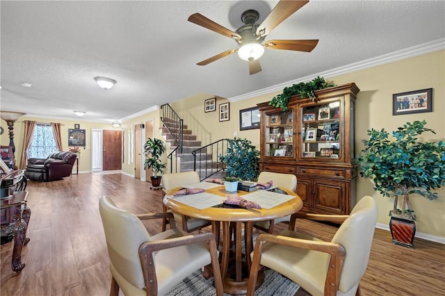 dining area featuring a textured ceiling, wood finished floors, baseboards, stairs, and crown molding