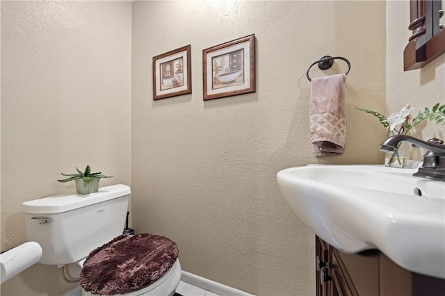 half bathroom featuring toilet, a textured wall, and a sink