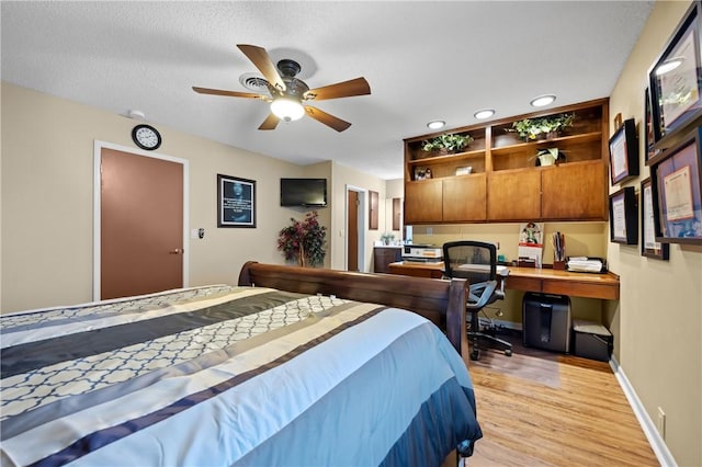 bedroom featuring a textured ceiling, built in desk, light wood-type flooring, and baseboards