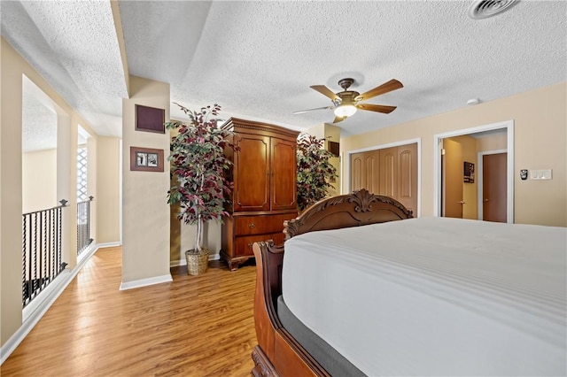 bedroom featuring light wood-type flooring, baseboards, visible vents, and a textured ceiling