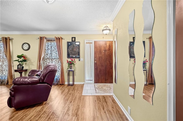 foyer featuring baseboards, a textured ceiling, ornamental molding, and wood finished floors