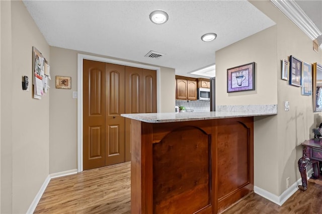 kitchen with light wood finished floors, stainless steel microwave, visible vents, brown cabinetry, and a peninsula