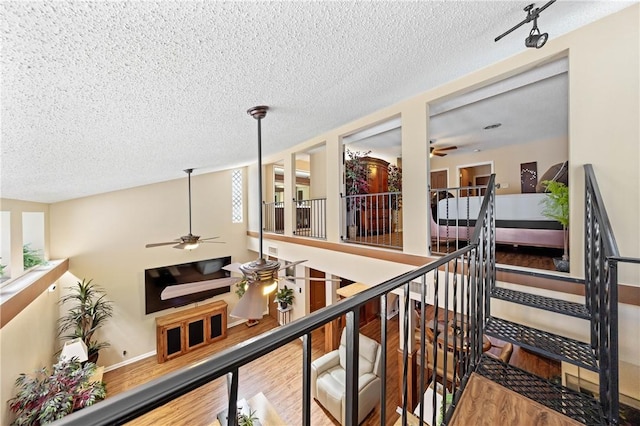 hallway featuring baseboards, a textured ceiling, an upstairs landing, and wood finished floors