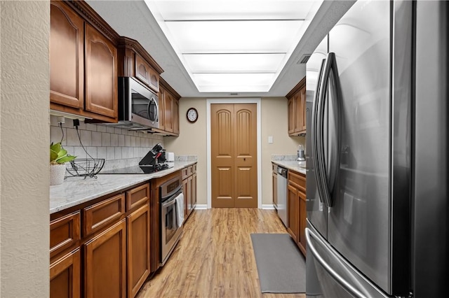 kitchen featuring light stone counters, light wood-style floors, appliances with stainless steel finishes, decorative backsplash, and brown cabinets