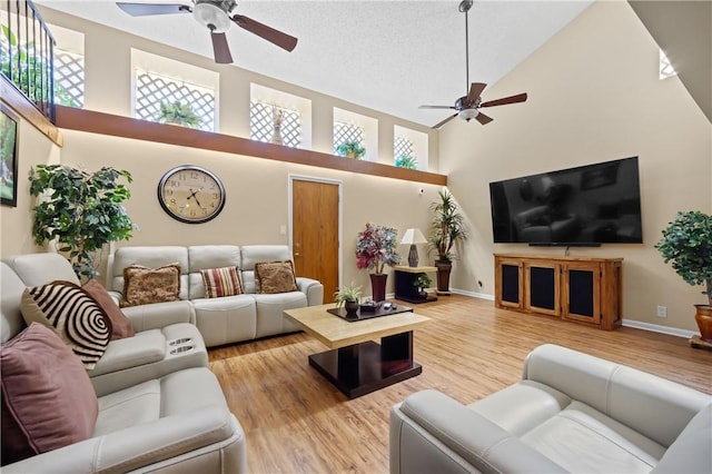 living room with a ceiling fan, high vaulted ceiling, light wood-style flooring, and baseboards