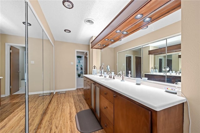 bathroom with visible vents, a textured ceiling, vanity, wood finished floors, and baseboards