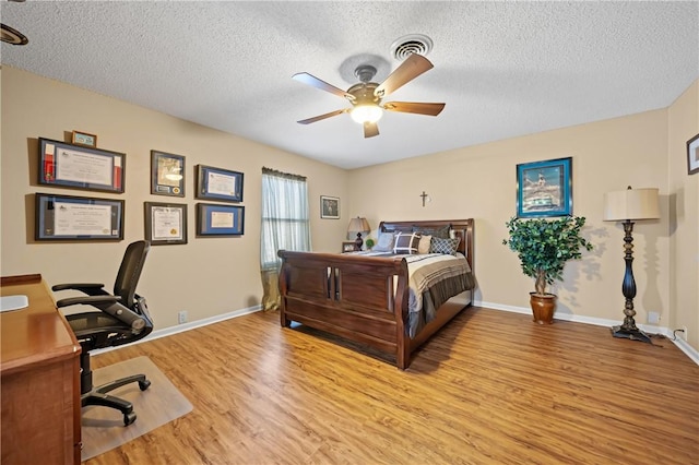 bedroom with baseboards, visible vents, light wood-style flooring, ceiling fan, and a textured ceiling