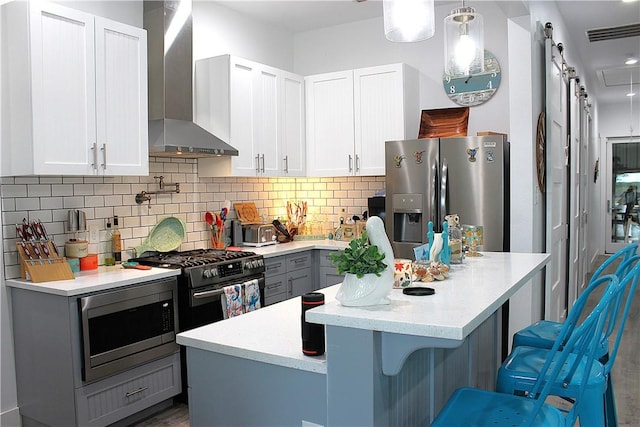 kitchen featuring white cabinetry, stainless steel appliances, gray cabinetry, wall chimney range hood, and a kitchen island