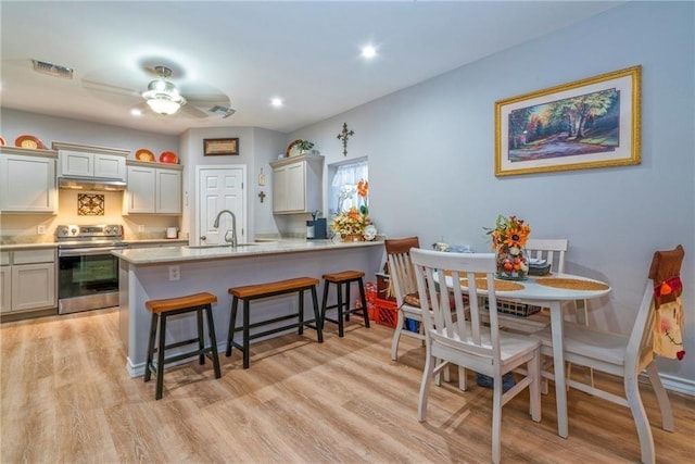 kitchen featuring a kitchen bar, sink, light hardwood / wood-style flooring, electric range, and kitchen peninsula