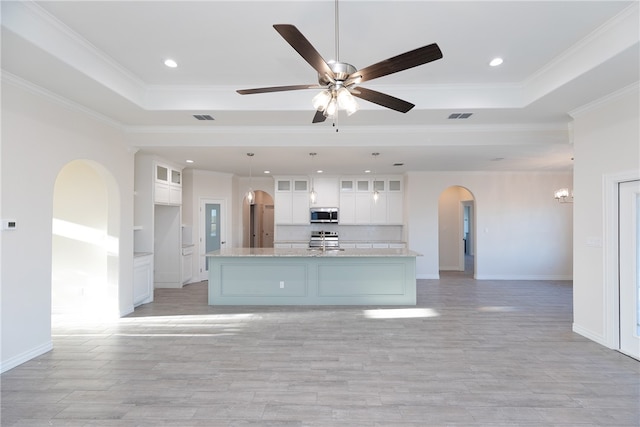 kitchen with appliances with stainless steel finishes, a tray ceiling, white cabinetry, and ornamental molding