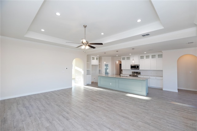 kitchen featuring white cabinets, appliances with stainless steel finishes, a tray ceiling, and a kitchen island with sink