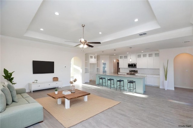 living room with ceiling fan, light wood-type flooring, crown molding, and a tray ceiling