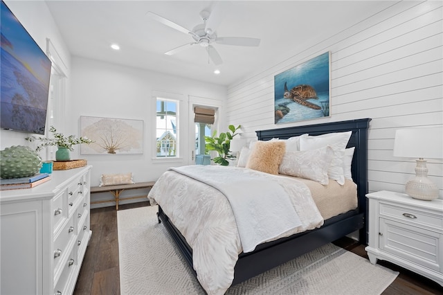 bedroom featuring ceiling fan, dark hardwood / wood-style flooring, and wooden walls