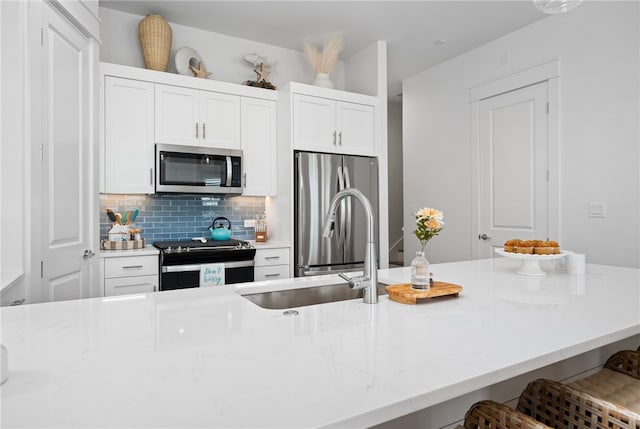 kitchen featuring appliances with stainless steel finishes, white cabinetry, decorative backsplash, sink, and a breakfast bar area