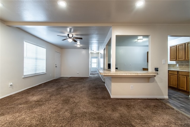 unfurnished living room featuring ceiling fan, crown molding, and dark carpet