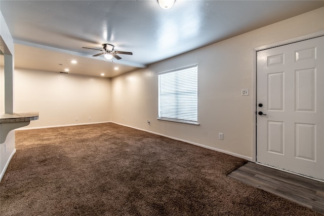 unfurnished living room featuring ceiling fan and dark colored carpet