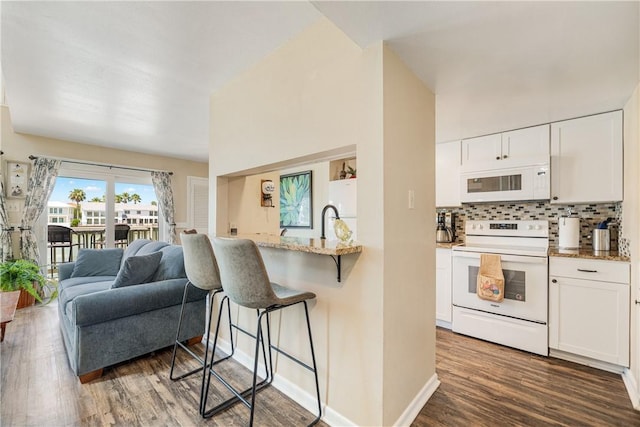 14300 Aloha St Unit 134, Corpus Christi, TX 78418 - kitchen with white appliances, a breakfast bar area, dark wood finished floors, white cabinetry, and tasteful backsplash