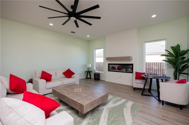 living area featuring a large fireplace, visible vents, wood finished floors, and a wealth of natural light