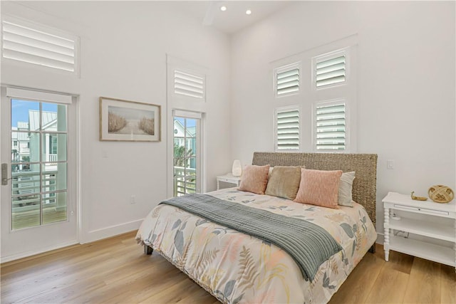 bedroom with multiple windows, access to exterior, a towering ceiling, and light hardwood / wood-style floors