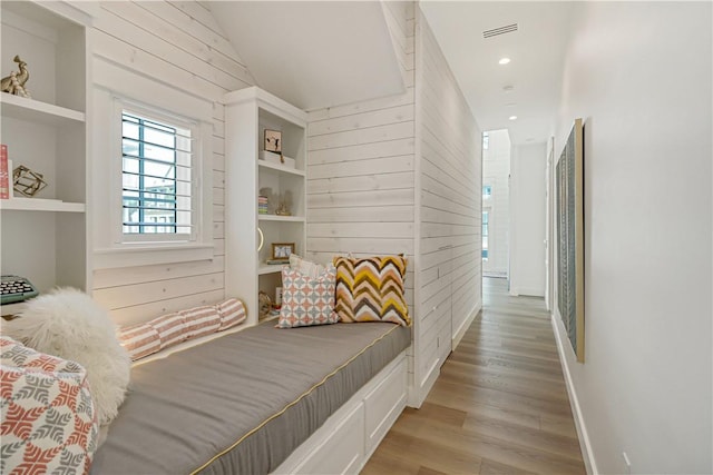 bedroom featuring wooden walls, vaulted ceiling, and light hardwood / wood-style flooring