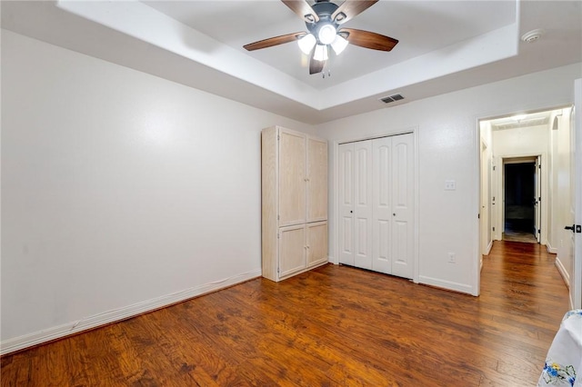 unfurnished bedroom featuring dark hardwood / wood-style flooring, a closet, a raised ceiling, and ceiling fan