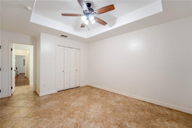 unfurnished bedroom with ceiling fan, a raised ceiling, and a closet