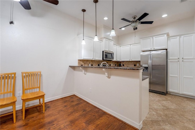 kitchen with kitchen peninsula, appliances with stainless steel finishes, a kitchen breakfast bar, white cabinetry, and hanging light fixtures