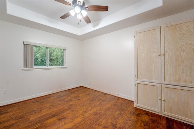 unfurnished room with dark hardwood / wood-style flooring, ceiling fan, and a raised ceiling