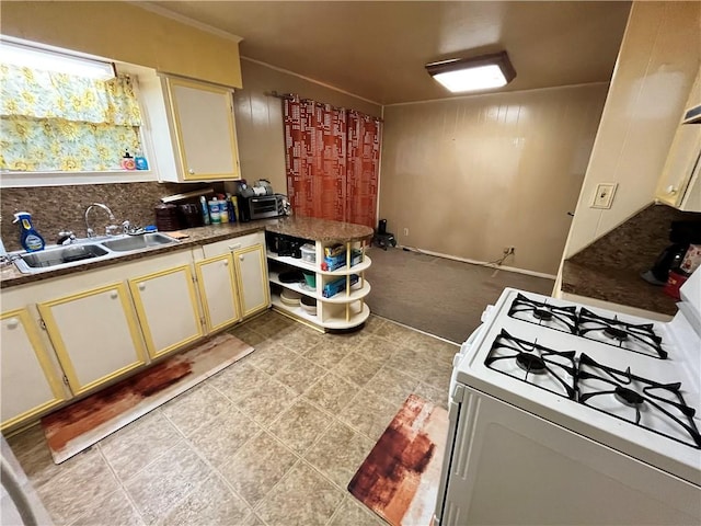 kitchen with cream cabinetry, backsplash, white gas stove, and sink