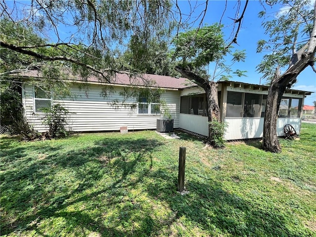 rear view of property featuring a sunroom, central air condition unit, and a lawn