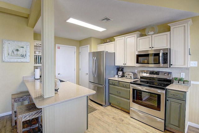 kitchen with appliances with stainless steel finishes, a breakfast bar area, green cabinetry, light wood-type flooring, and decorative backsplash