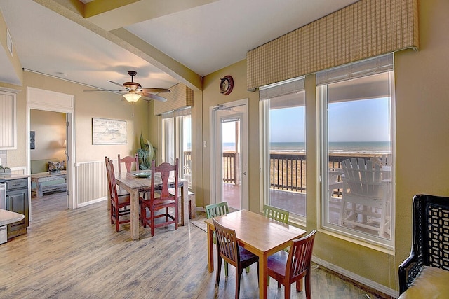 dining space with ceiling fan, a water view, light hardwood / wood-style floors, and beamed ceiling