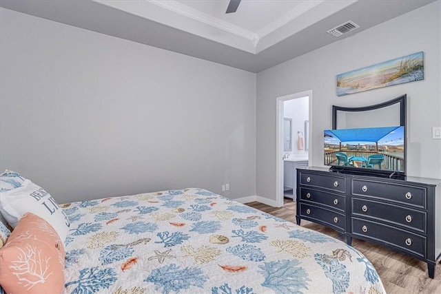 bedroom featuring a ceiling fan, wood finished floors, visible vents, a tray ceiling, and crown molding