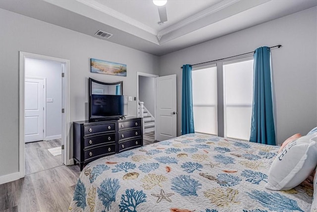 bedroom featuring visible vents, a tray ceiling, wood finished floors, crown molding, and baseboards