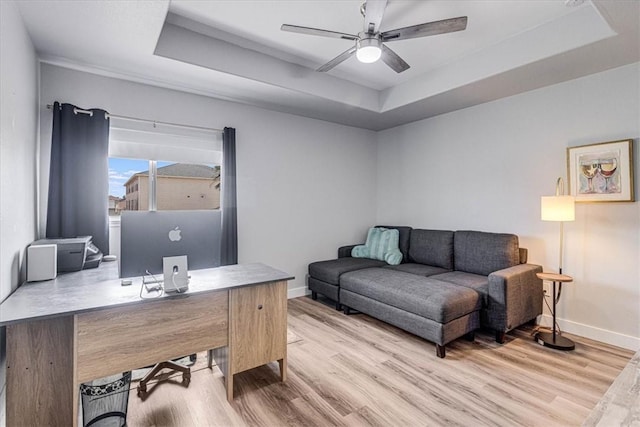 home office with a tray ceiling, wood finished floors, baseboards, and ceiling fan