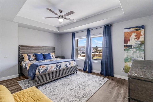 bedroom featuring baseboards, a tray ceiling, and wood finished floors